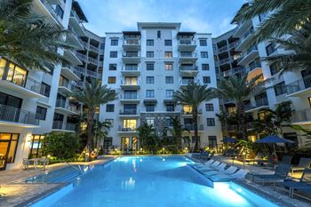 A swimming pool in front of a white apartment building surrounded by palm trees at Mayla Pompano, FL, 33062